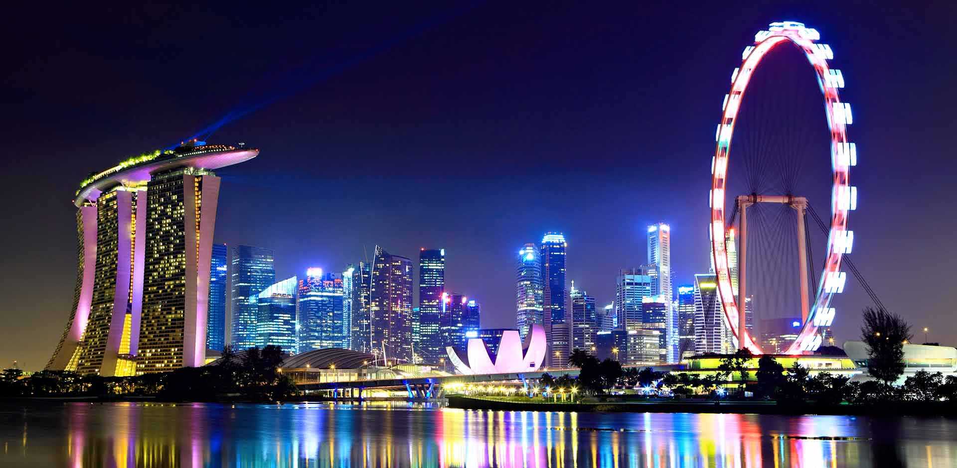 Singapore skyline at night with Marina Bay Sands, the downtown core, and the illuminated Singapore Flyer reflected across Marina Bay